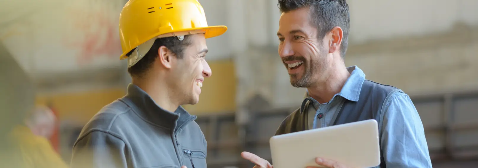 Two warehouse workers are referencing something on a tablet.