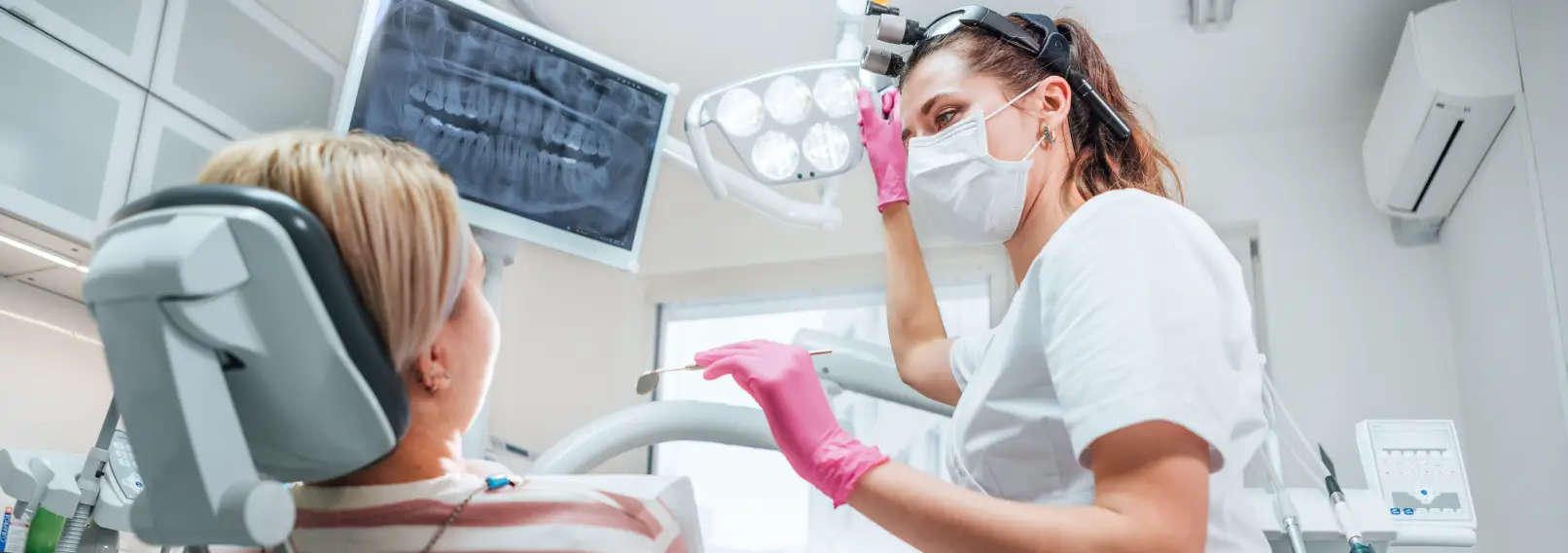 Dental hygienist adjusting the overhead light to examine a patient.