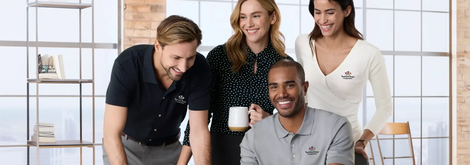 Four colleagues in branded shirts collaborating around a workspace, showing how a hybrid team uniform program maintains brand consistency