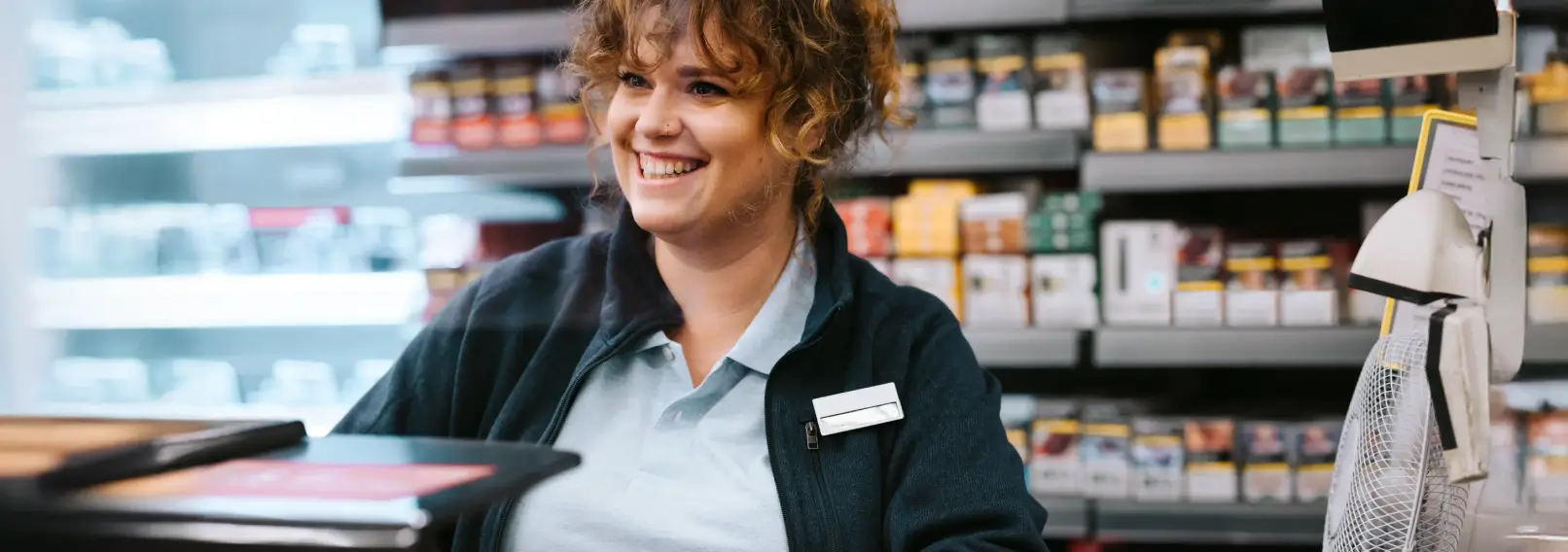 A pharmacist wearing a polo and a fleece jacket behind a checkout counter.