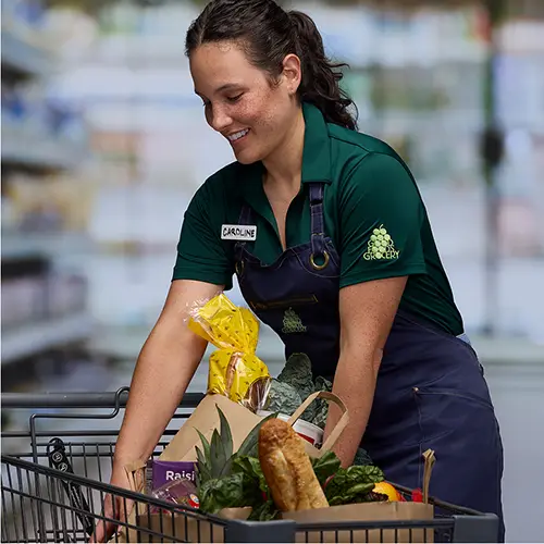 A grocery store employee filling a cart with items.
