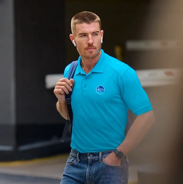 Man wearing a blue monogrammed polo and carrying a backpack