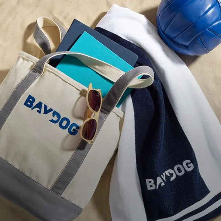 Monogrammed tote and towel on a beach alongside sunglasses, notebooks and a volleyball
