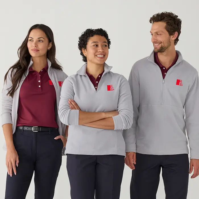 Three employees wearing matching gray sweaters with their organization's logo custom embroidered.