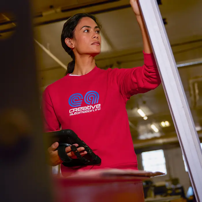A woman holding a tablet wearing a red sweater with a custom logo on it.